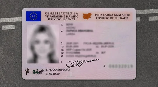 Bulgarian driving license card on a gray surface, shows a blurred photo, text blocks, and a signature area on the bottom right side.
